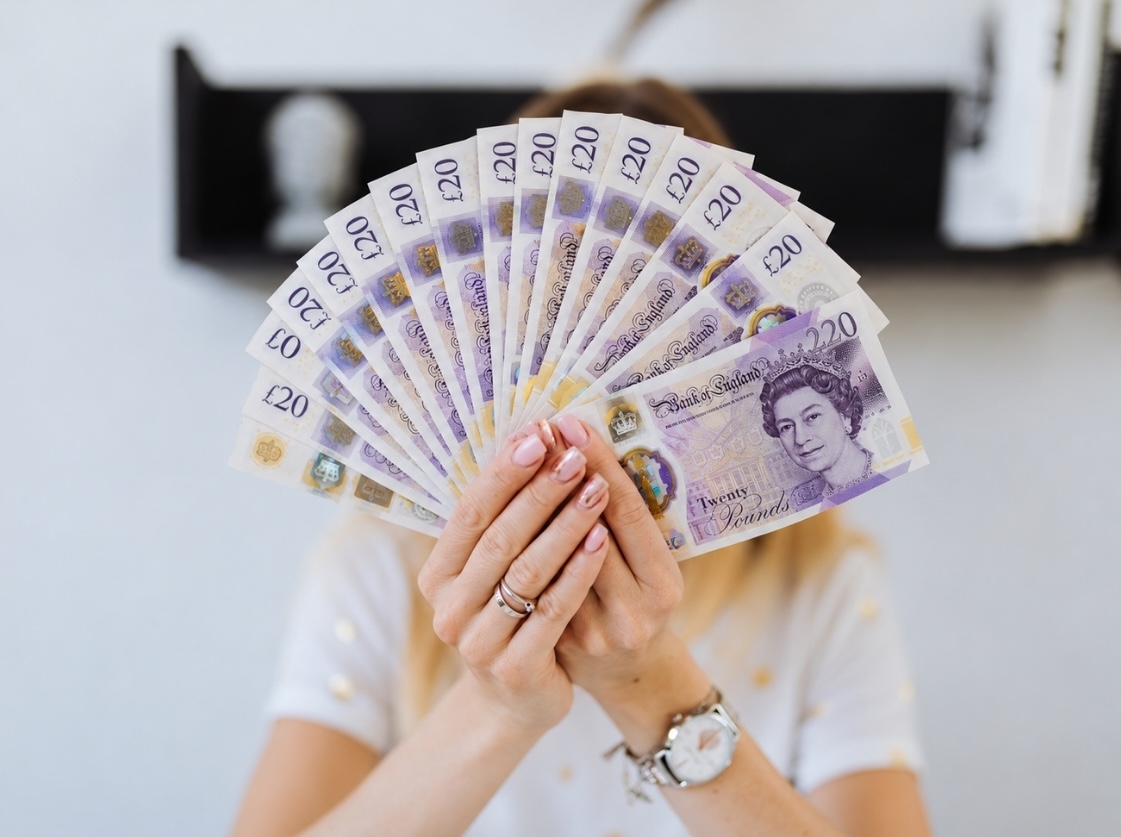 Creative holding a pile of fanned £20 bank notes in her hand to represent cash in business